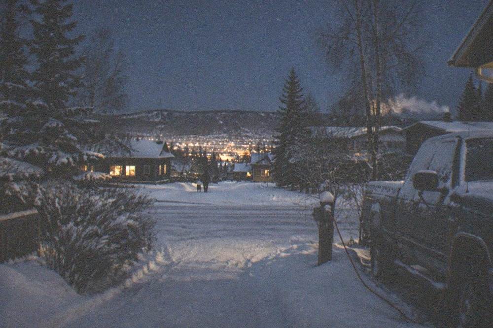 A quiet snowy street in a Fairbanks neighborhood with warm light from windows and a clear starry sky
