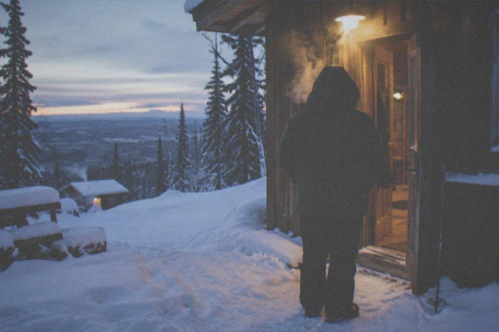 A warmly dressed guest waiting outside a lit lodge doorway on a deep winter night